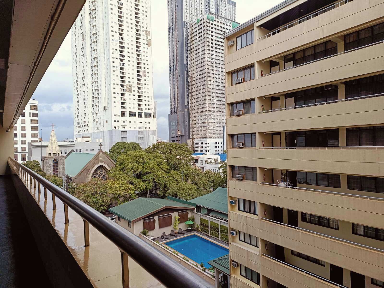 A view from a balcony overlooking a swimming pool, with tall buildings and a church in the background.