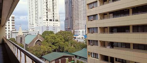 A view from a balcony overlooking a swimming pool, with tall buildings and a church in the background.