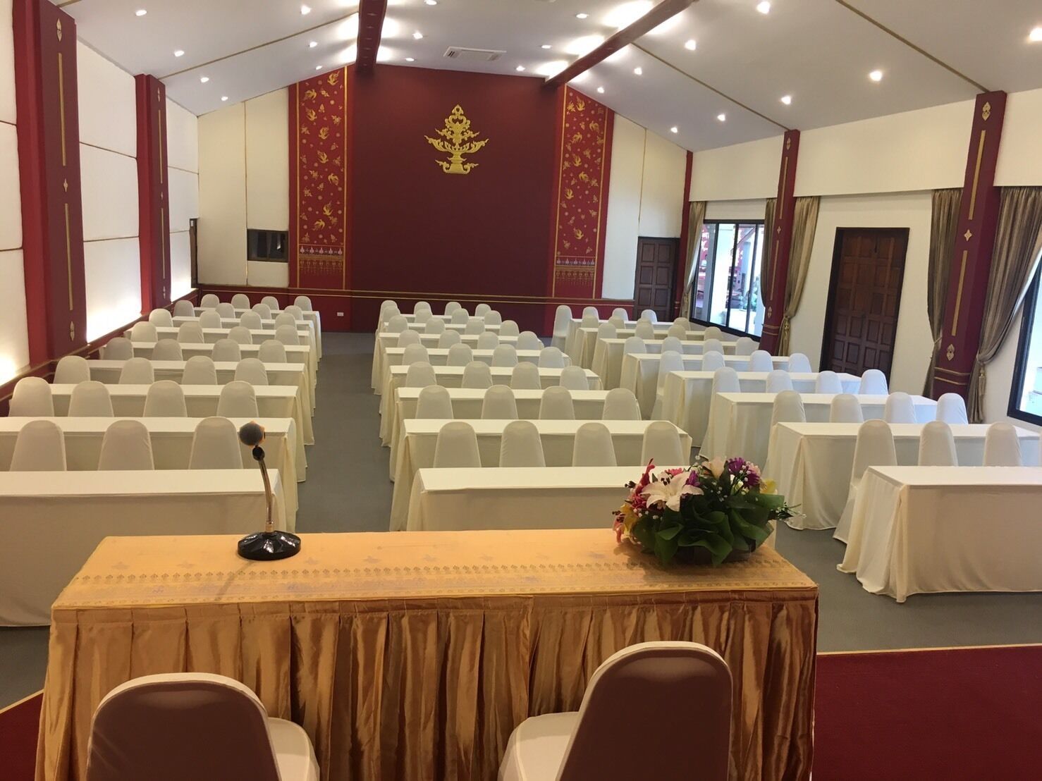 A conference room with rows of white chairs and tables, a podium, and a floral arrangement on one table.