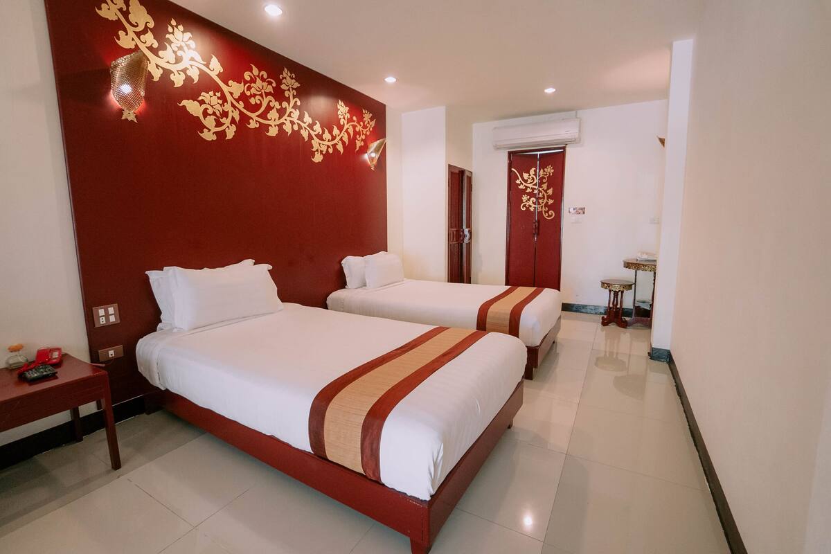 Habitación de hotel con dos camas, una pared de acento roja y una mesita con una lámpara.