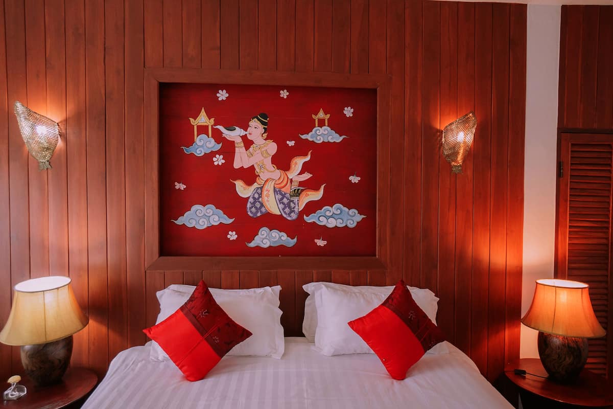 Habitación de hotel con cama, almohadas rojas y blancas, un mural en la pared y dos lámparas en mesitas de noche.