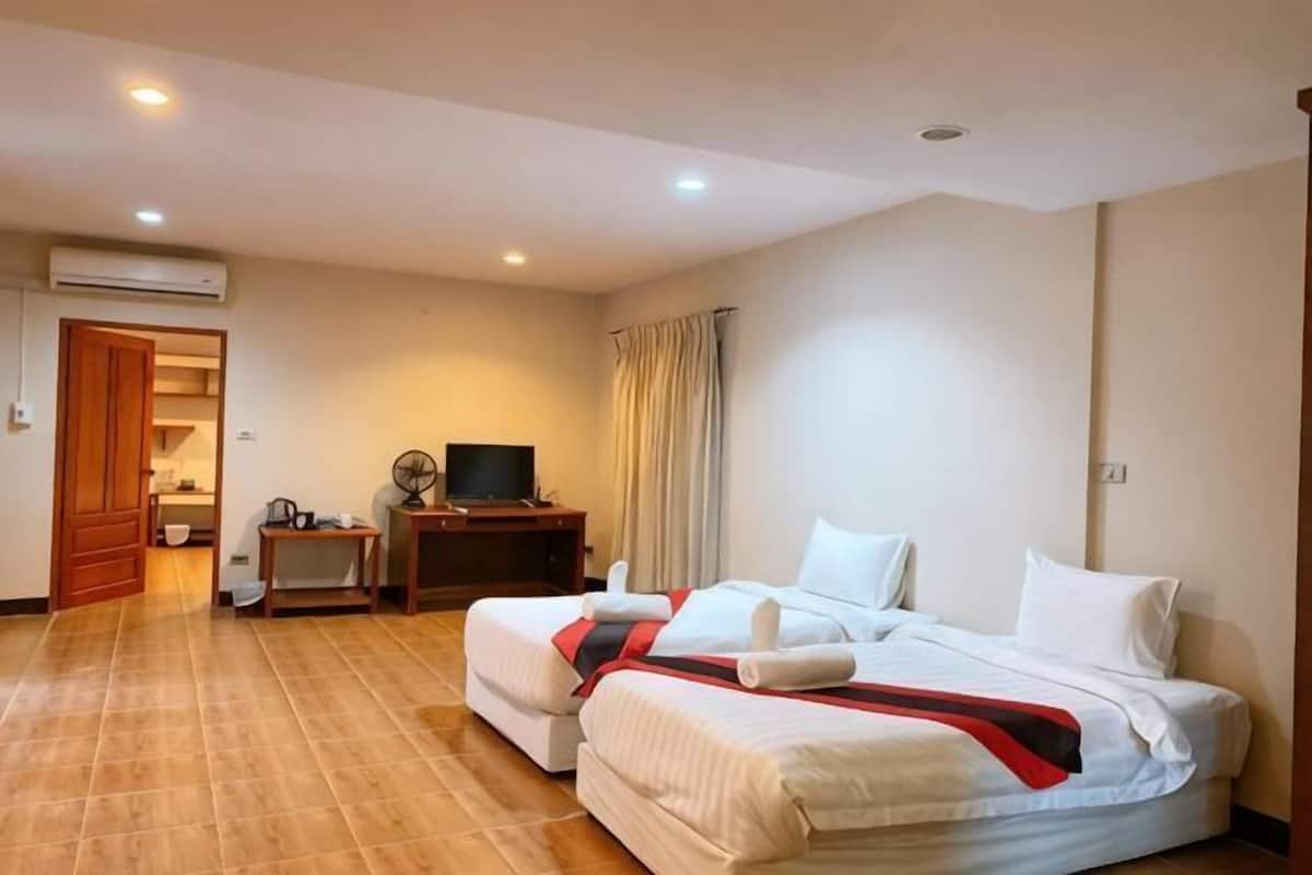 Habitación de hotel con dos camas, televisión, escritorio y baño visible a través de una puerta abierta.