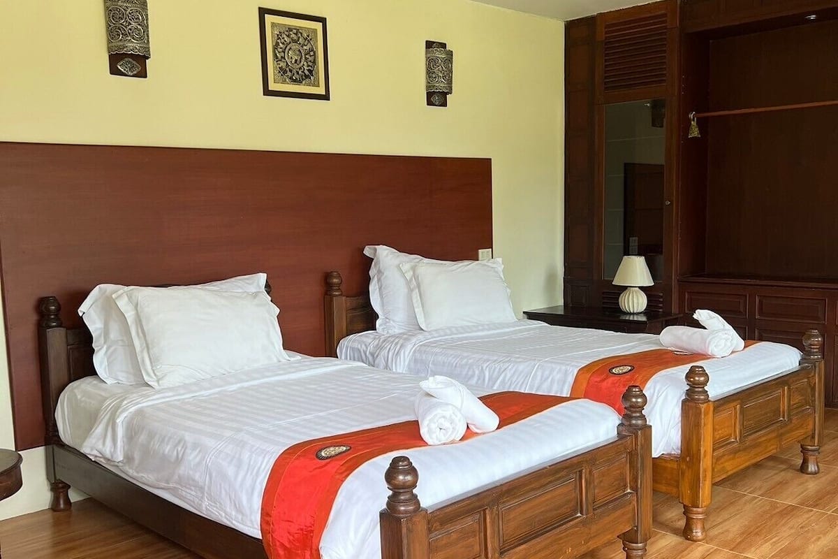 Una habitación de hotel con dos camas de madera, cabeceros de madera, piso de madera y una puerta de madera.