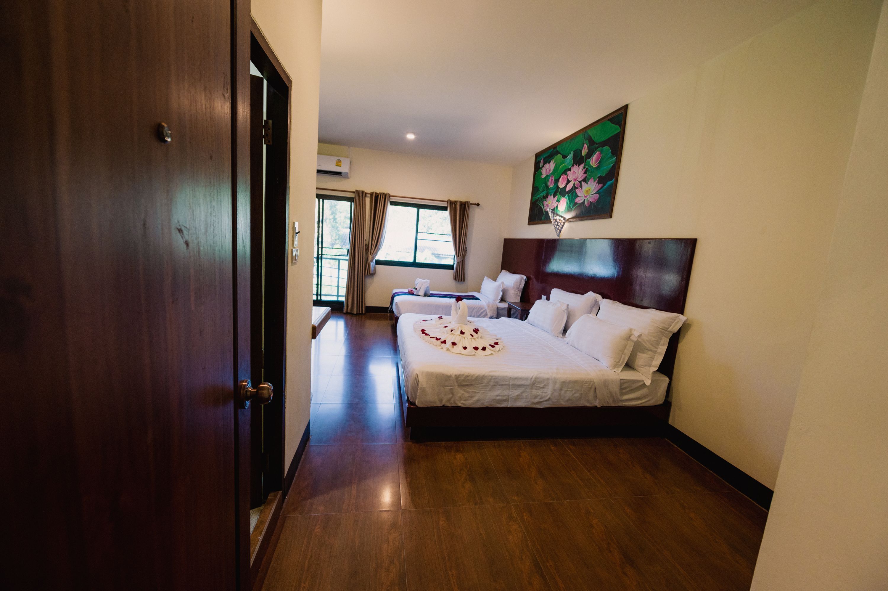 A hotel room with a large bed, a wooden floor, a painting on the wall, and a window with curtains.