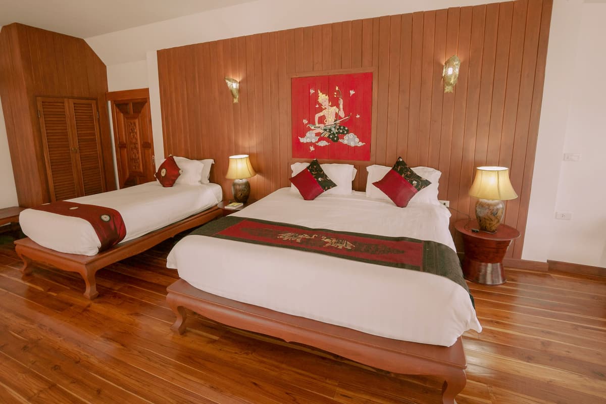 Habitación de hotel con dos camas de madera, un armario de madera, un adorno rojo en la pared y dos lámparas de noche.