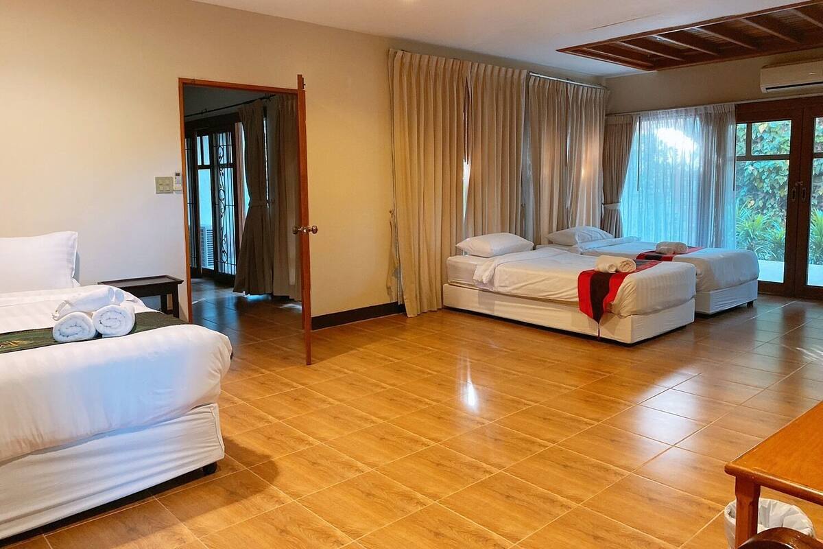 Habitación de hotel con dos camas, piso de madera y vistas a la vegetación por las ventanas.
