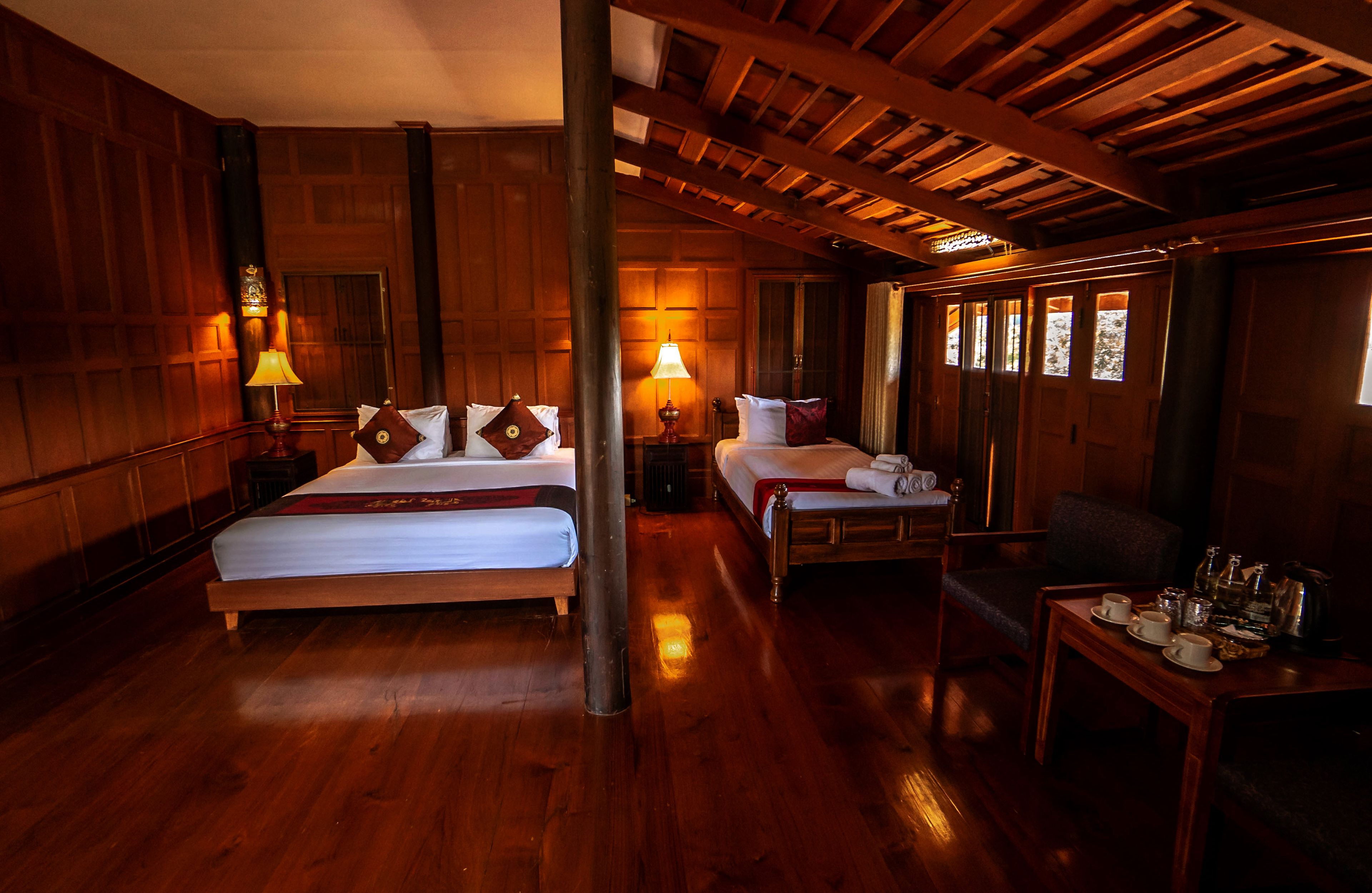 A wooden-floored room with two beds, a table with cups and a kettle, and a chair.