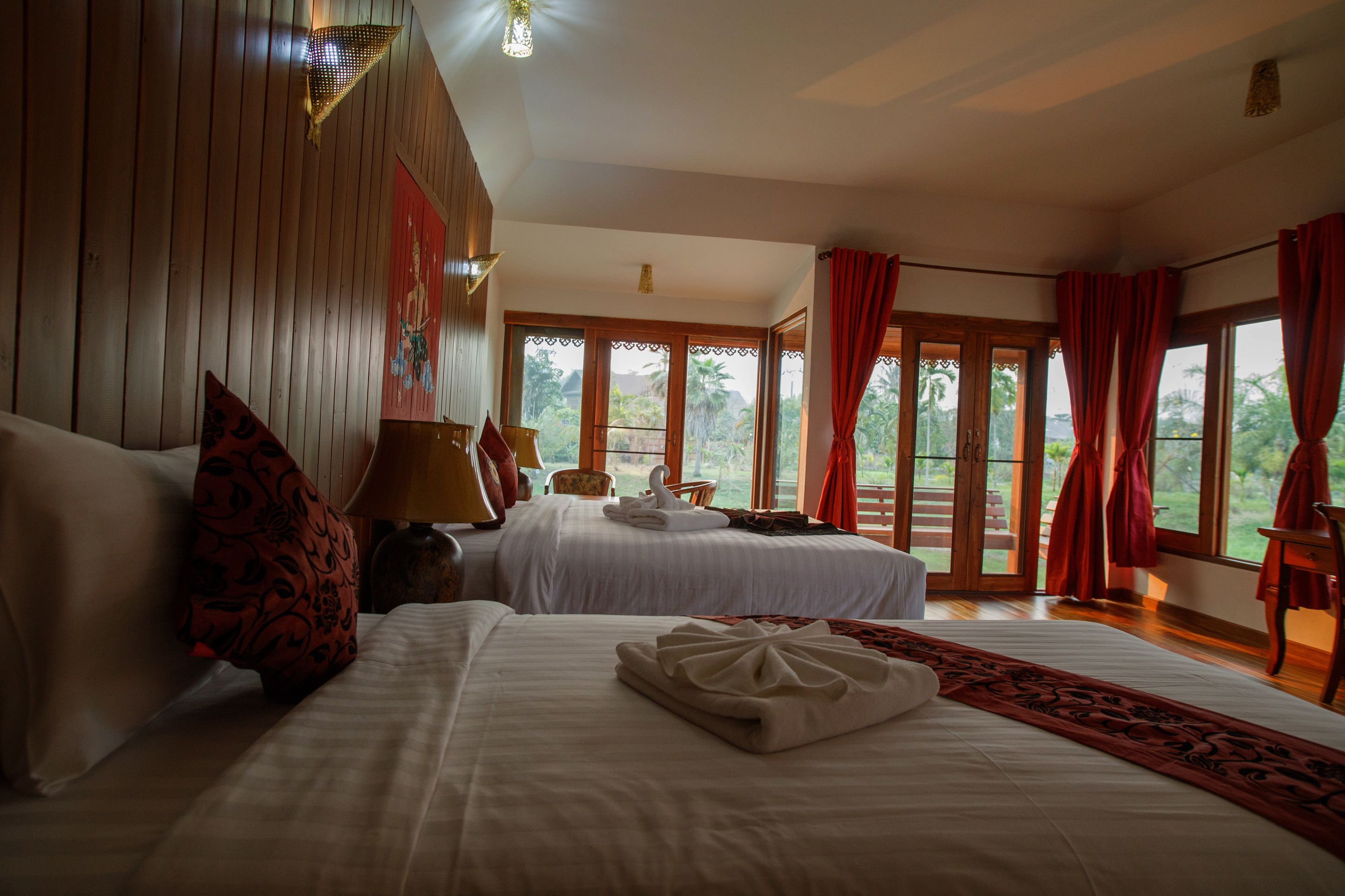 Habitación de hotel con dos camas, un ventanal con cortinas, techo de madera y vistas al exterior.