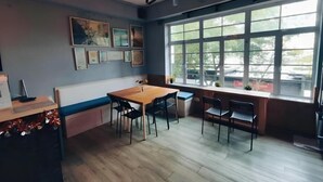 A dining area with a wooden table and chairs, a ceiling fan, large windows, and wall-mounted artwork.