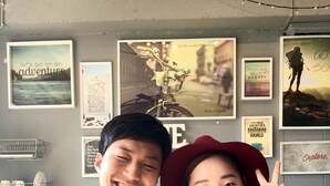 Two people posing in front of a wall with various framed pictures and motivational quotes.