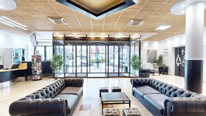 A modern lobby with leather sofas, a reception desk, and a large glass door leading outside. - Résidence Internationale de Paris (Paris)