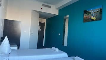 Een hotelkamer met twee bedden, een muur in teal, een schilderij van een brug en een deur naar een andere kamer.