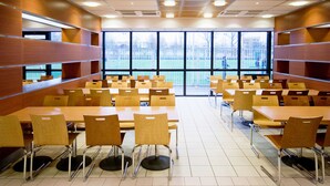 En cafeteria med flera bord och stolar, stora fönster och utsikt över en lekplats utanför.