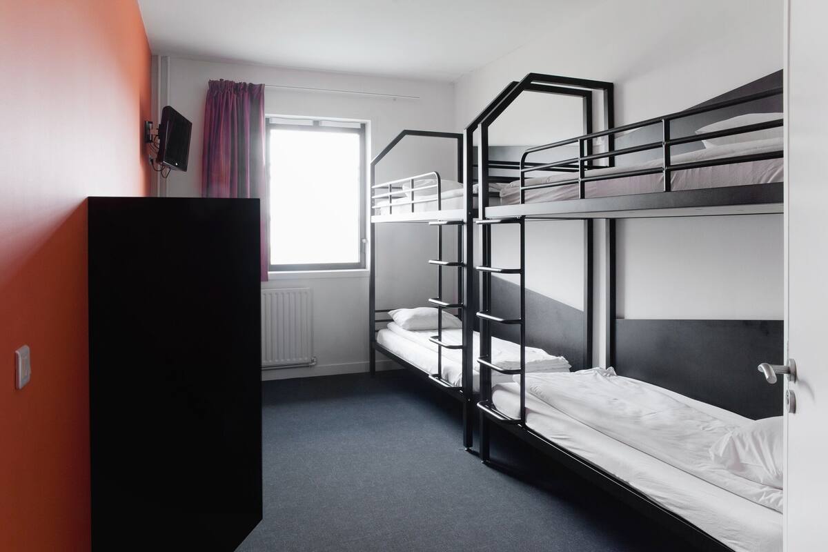 Un dormitorio con literas, una ventana con cortinas, un radiador y un armario negro.