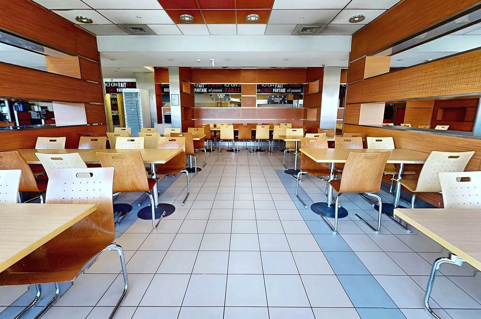 Una cafetería con varias mesas y sillas, piso de baldosas y una barra con un cartel de menú.