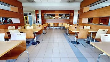 Una cafetería con varias mesas y sillas, piso de baldosas y una barra con un cartel de menú.