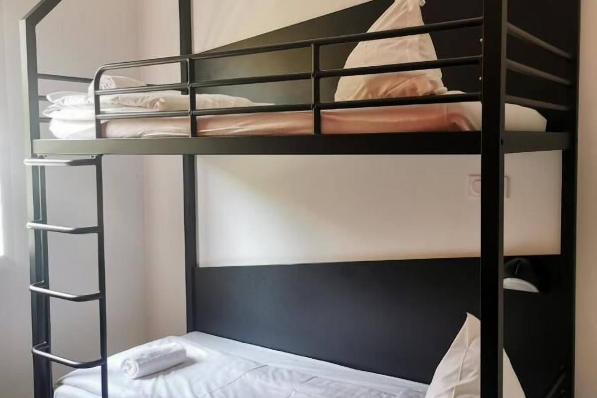 Una litera con escalera, ropa de cama blanca y cabecera negra.