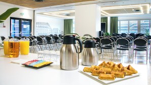 A breakfast setup with coffee pots, juice glasses, and pastries on a table in a room with chairs and a view of buildings. - Résidence Internationale de Paris (Paris)