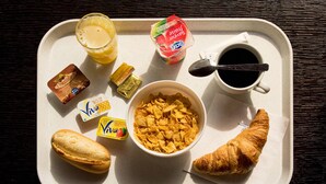Ett bricka med frukosttillbehör, inklusive flingor, juice, yoghurt, kaffe och en croissant.