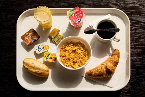 Una bandeja con alimentos para el desayuno, incluyendo cereal, jugo, yogur, café y un croissant.
