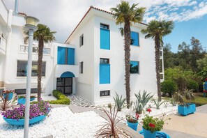 A white building with blue accents, palm trees, and potted plants. - Kamari Beach Hotel (Thasos)