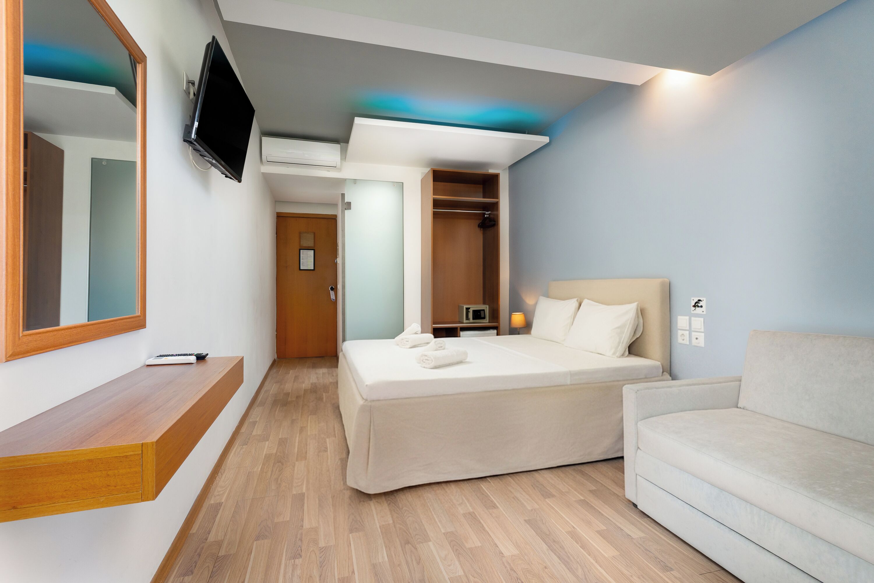 Una habitación de hotel con cama, televisor, sofá y banca de madera.