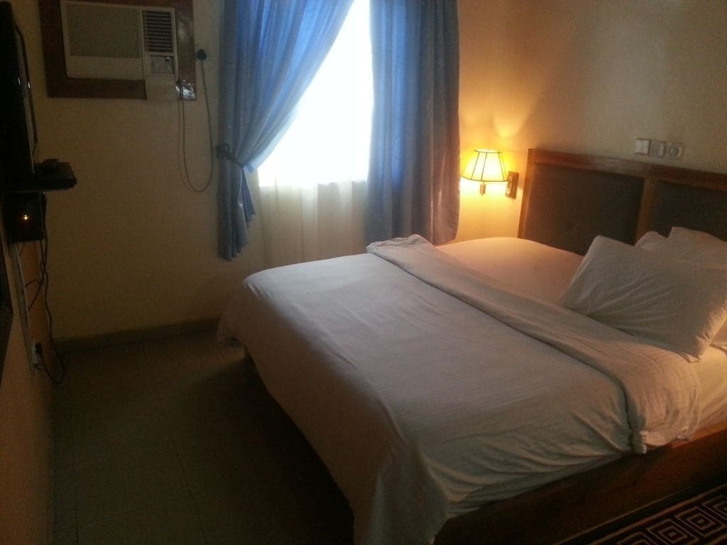 A hotel room with a bed, a lamp, and a window with curtains.