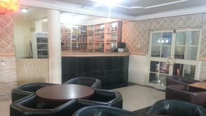 A bar area with multiple seating options, including round tables and cushioned chairs, and a shelving unit displaying various bottles. - Definite Destiny Asaba (Asaba)