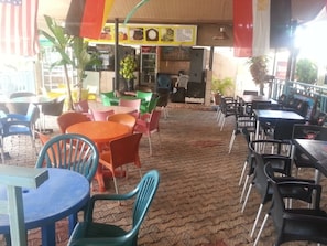 An outdoor cafe with tables and chairs, a menu board, and a brick floor.