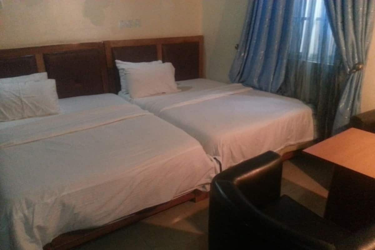 A hotel room with two single beds, a wooden headboard, a small table, and a black leather chair.