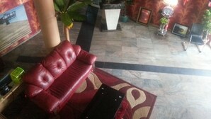 A lobby with a red leather sofa, a reception desk, a large potted plant, and a patterned carpet. - Definite Destiny Asaba (Asaba)