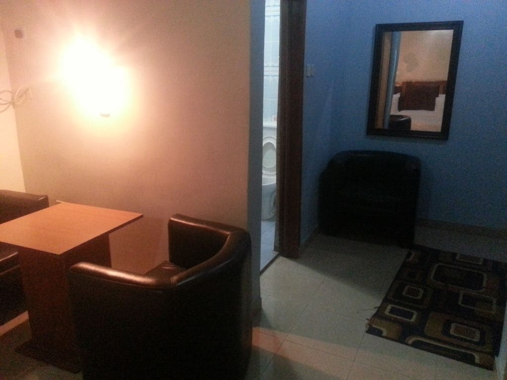 A room with a dining table, two chairs, a trash bin, a patterned rug, and a mirror on the wall.