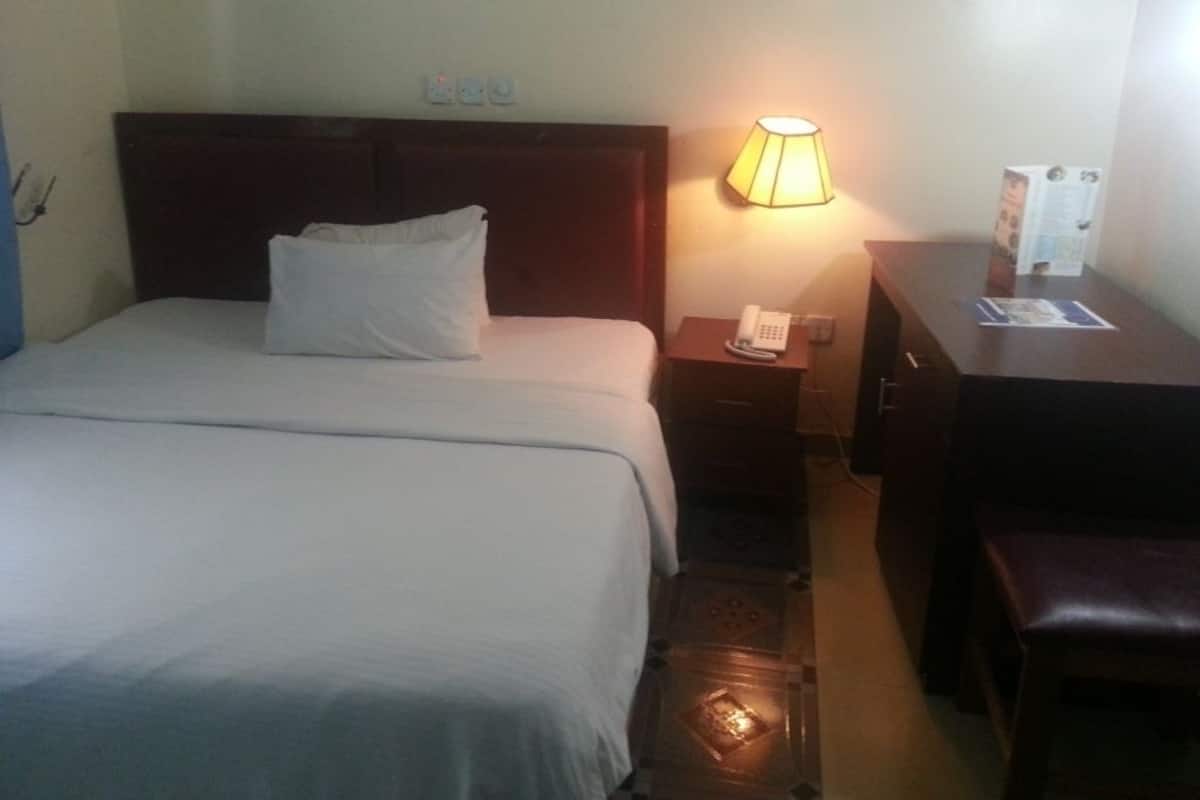 A hotel room with a bed, bedside lamp, nightstand, and a desk with a chair.