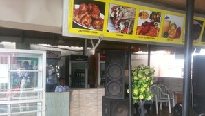 A restaurant with a menu board displaying food items like coated fried chicken and shawarma. There are speakers and a potted plant on the patio. - Definite Destiny Asaba (Asaba)