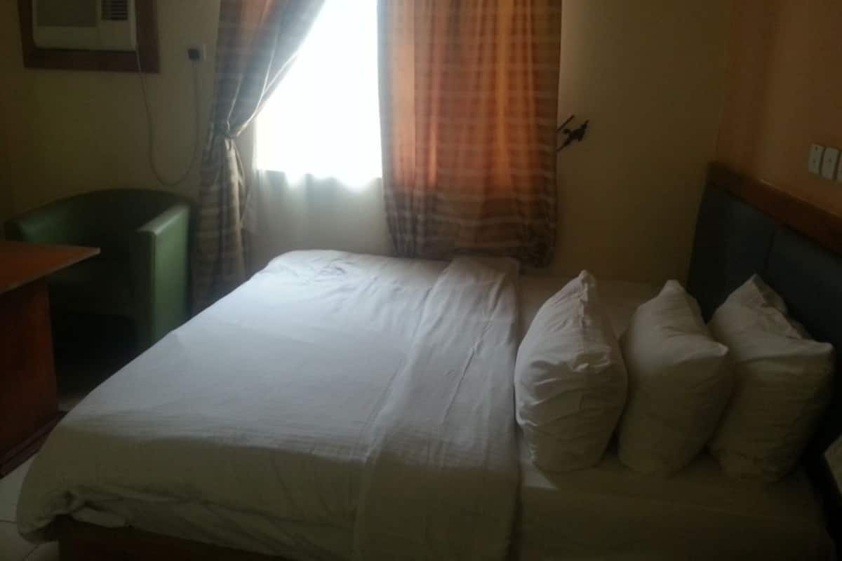 A hotel room with a bed, a desk, and a window with curtains.