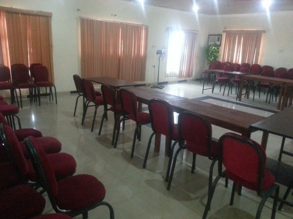 A conference room with multiple tables and red chairs, large windows with curtains, and a podium.
