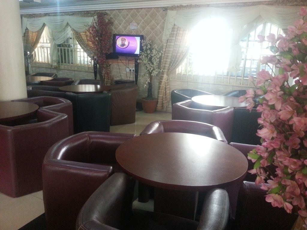 Un interior de restaurante con mesas redondas y asientos acolchados, una pantalla de televisión y una planta en maceta.