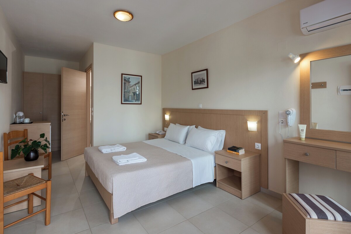 Habitació d'hotel amb llit, taulell de nit, cadira, escriptori i mirall.