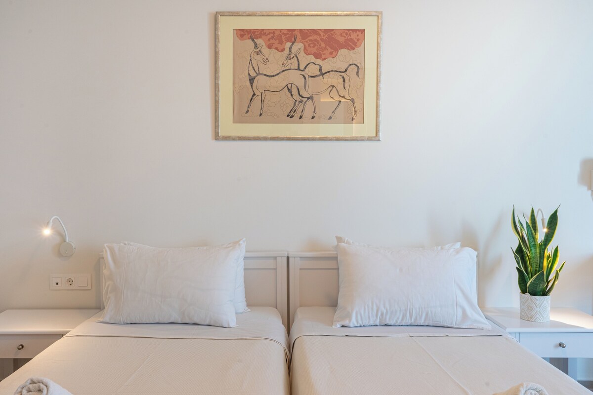 Habitació d'hotel amb dos llits, un quadre penjat a la pared, làmpades de nit, una taula de nit i una planta en test.