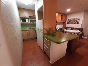 A compact kitchen with a microwave, cabinets, and a small dining area with a table and chairs. - Snow Comfort Edificio Monte Gorbea (Monachil)