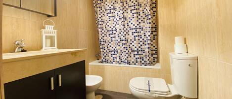 A bathroom with a toilet, a sink with a mirror, a shower curtain, and a toilet paper holder.