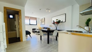 A modern kitchen with a built-in stove, a dining area with a table and chairs, and a living area with a sofa and a TV. - Snow Comfort Edificio Monte Gorbea (Monachil)
