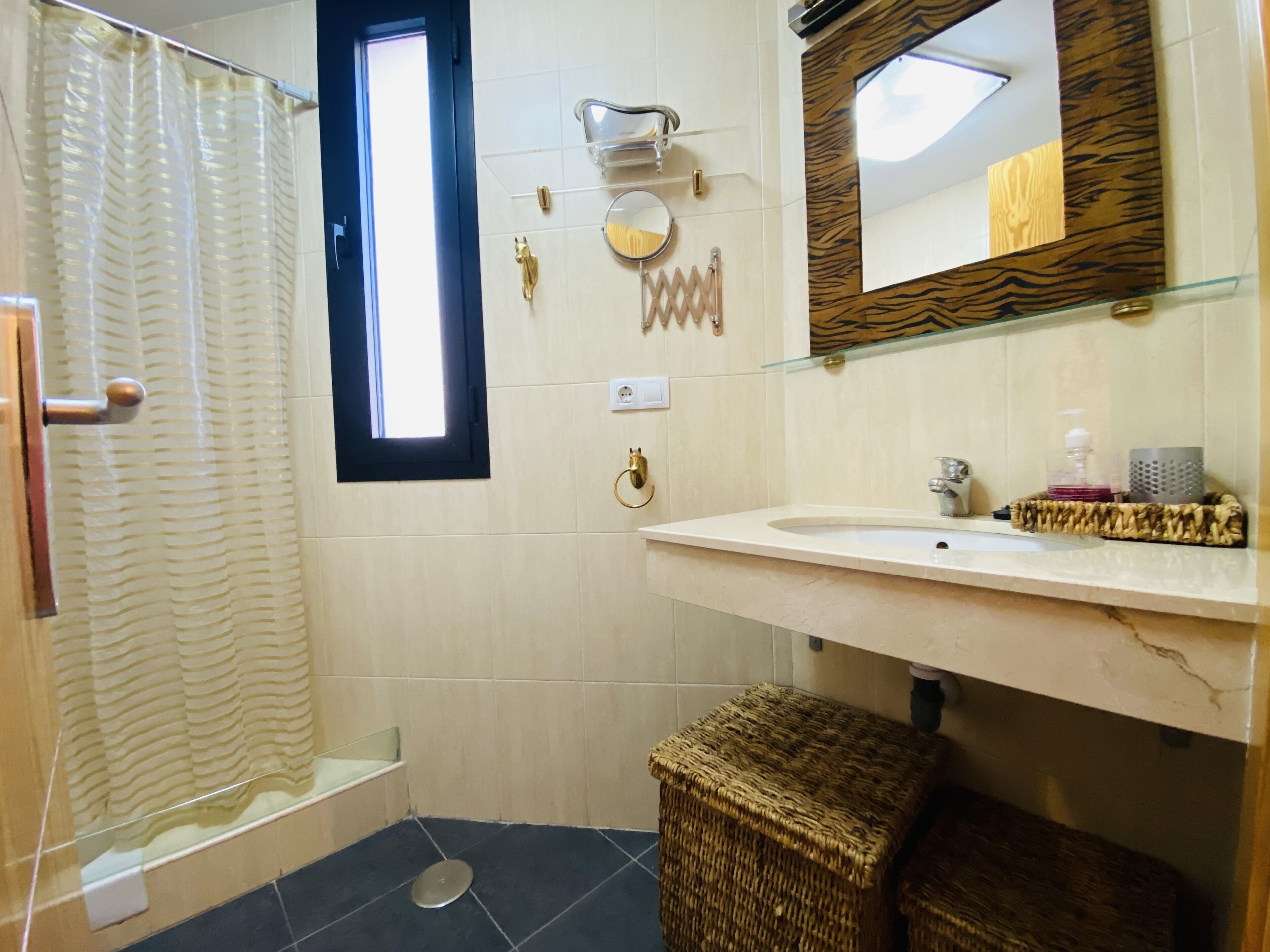 A bathroom with a shower, a sink, a mirror, and a small stool.