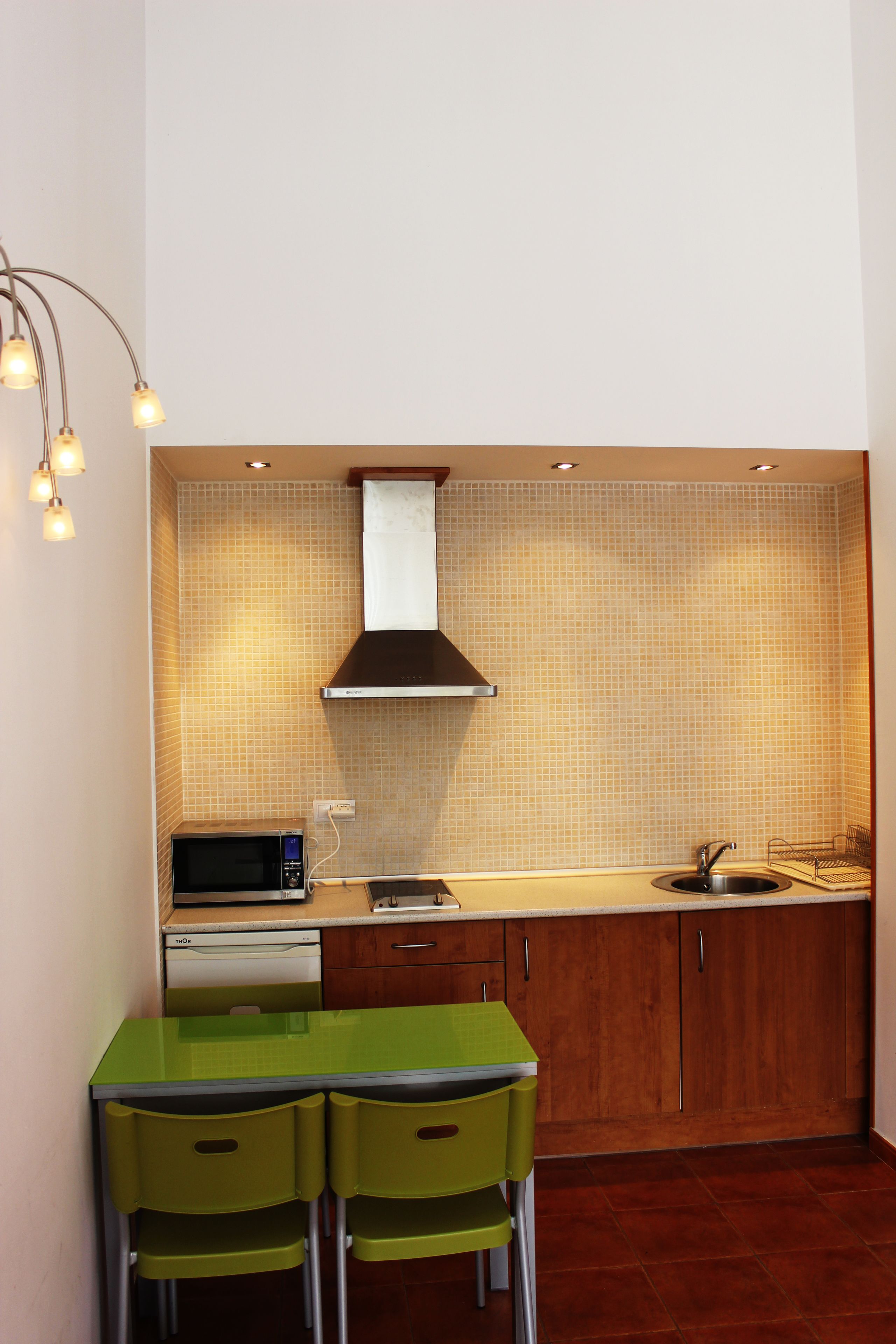 A compact kitchen with a microwave, sink, and green chairs.