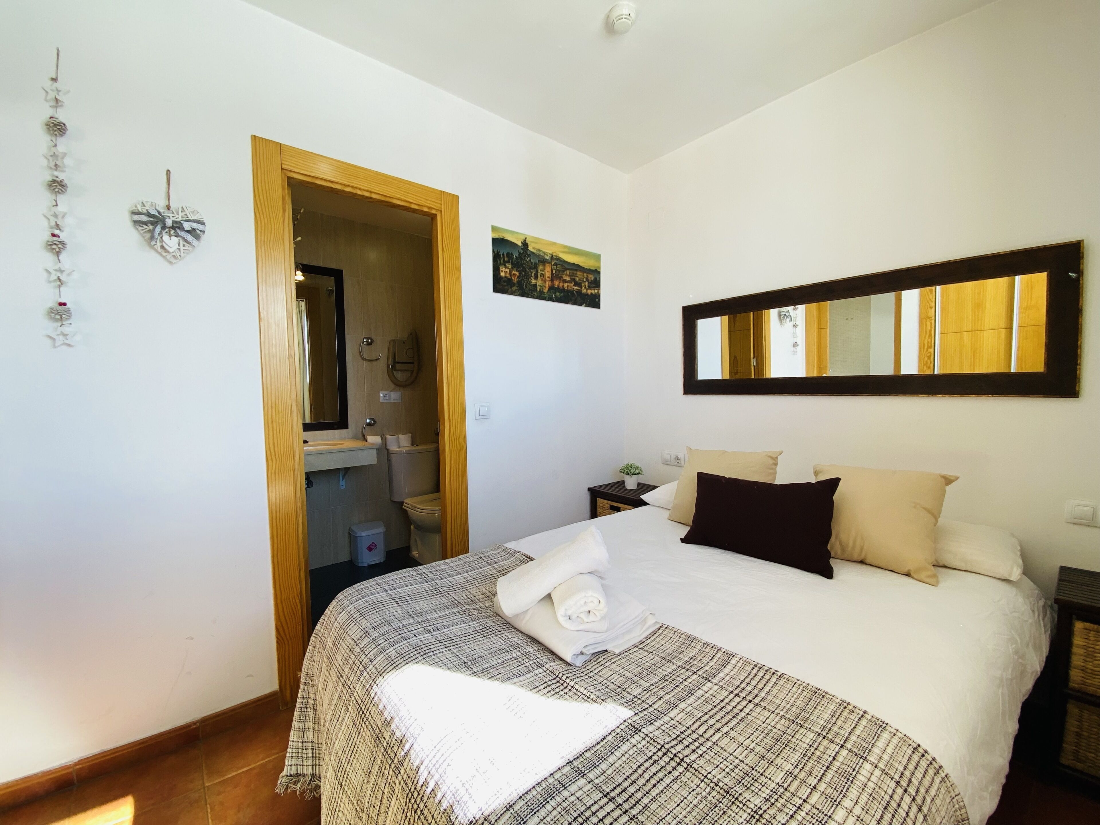 A bedroom with a bed, a nightstand, a mirror, a painting, and a door leading to a bathroom.