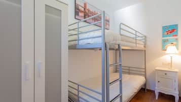A bunk bed room with a white wardrobe, a bedside table with a lamp, and two wall art pieces.