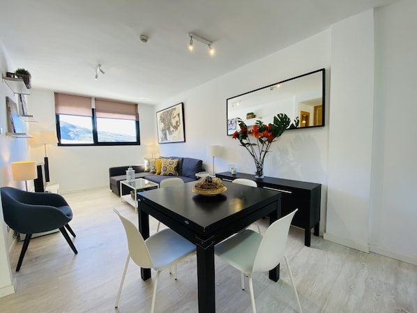 A modern living room with a dining area, featuring a sofa, a coffee table, and a dining table with chairs. - Snow Comfort Edificio Monte Gorbea (Monachil)