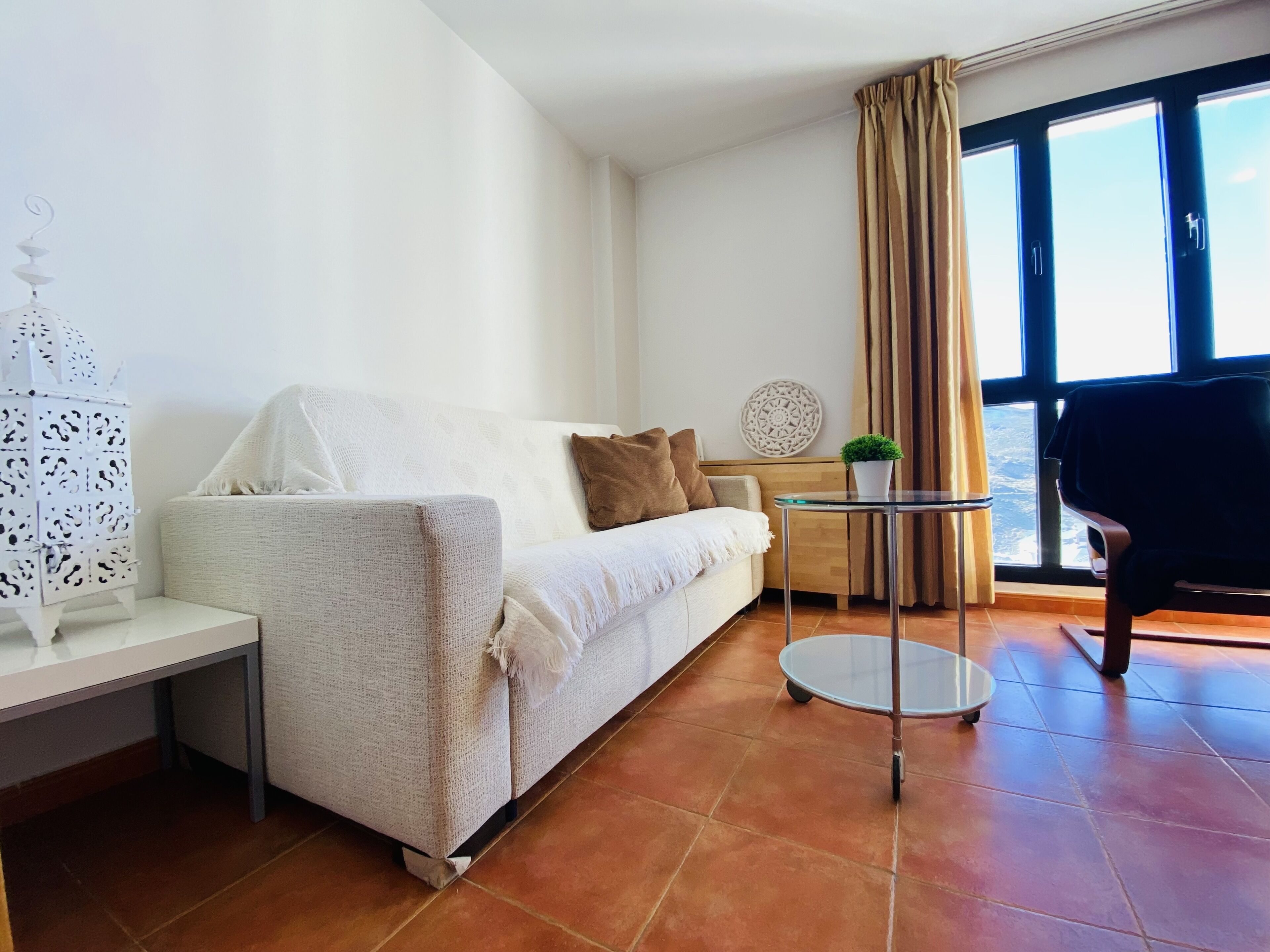 A modern living room with a white sofa, a small round table, and a view of the city through large windows.