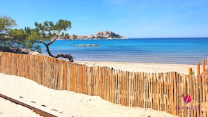 Una playa con una valla de madera, cielo azul cristalino y una isla rocosa a lo lejos.