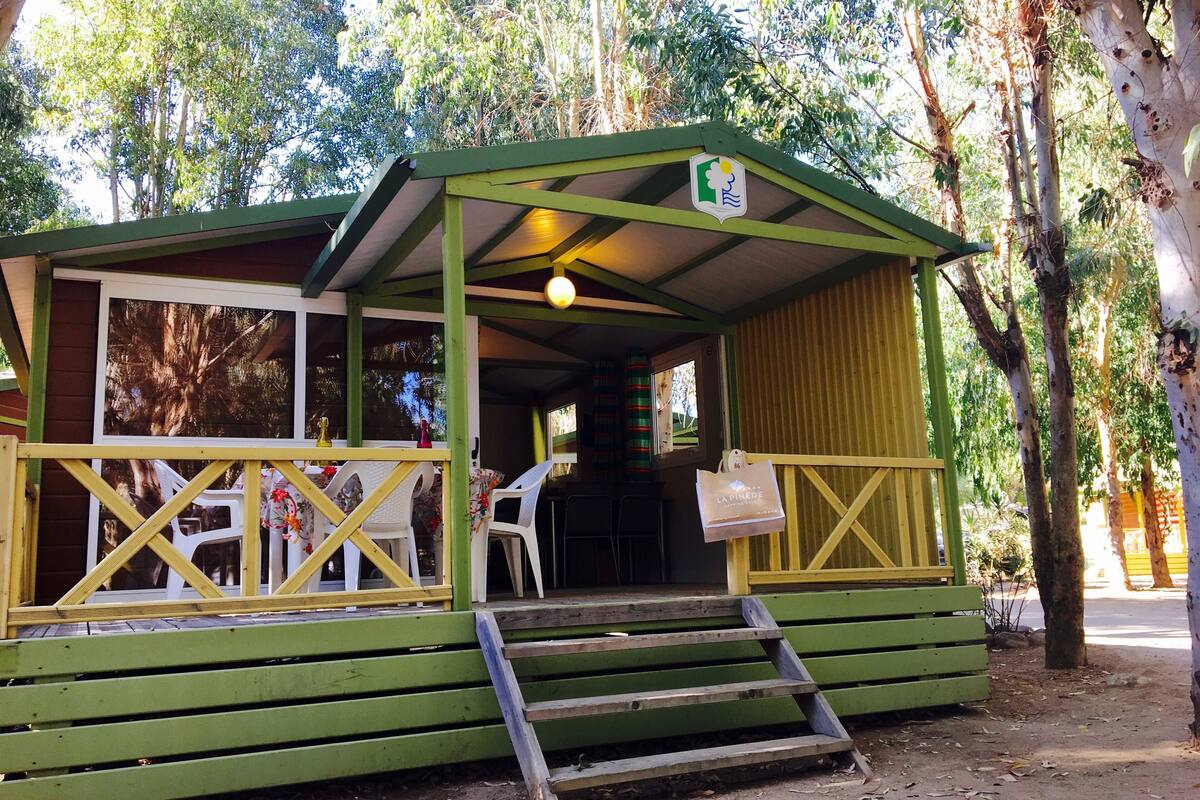 A small, green wooden structure with a porch and a staircase leading to an entrance.